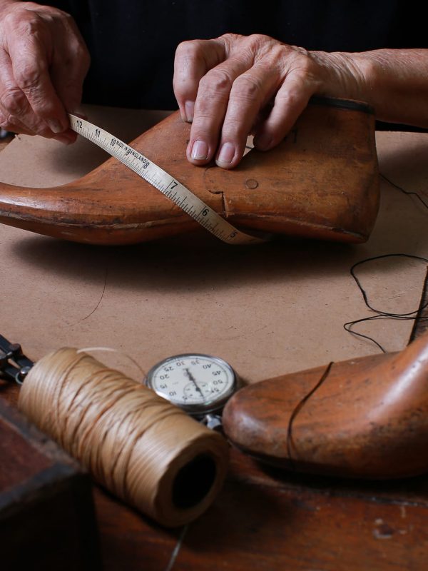 Shoemaker measuring a shoe with measure tape in workshop