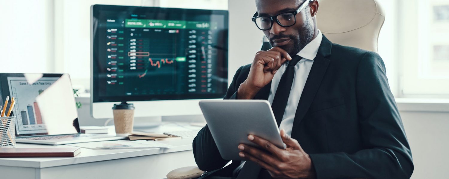 Concentrated young African man in formalwear using modern technologies while working in the office